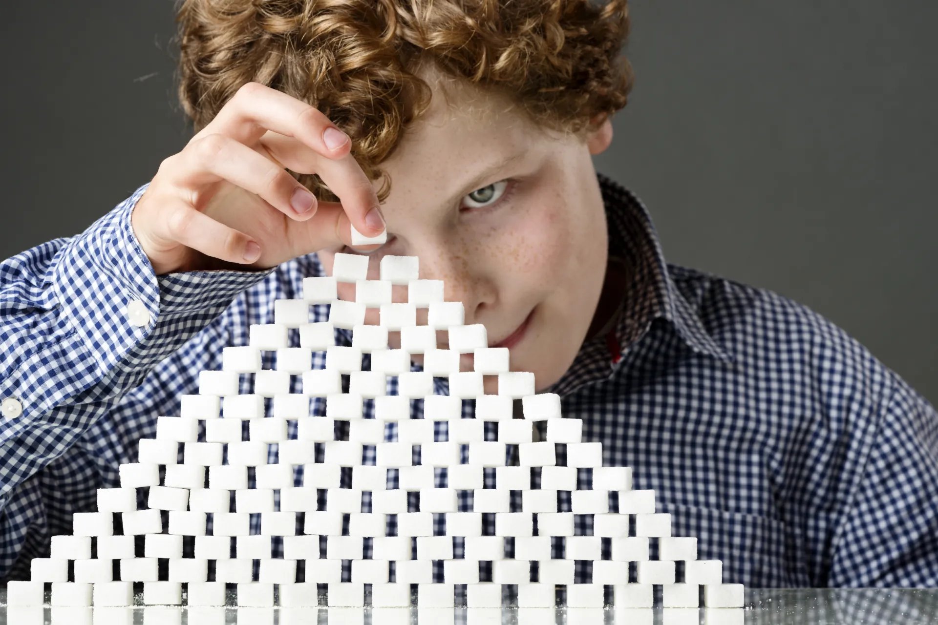 Überall steckt Zucker drin: Ein Junge baut eine Pyramide aus Zuckerwürfeln, die die Menge seines tägichen Zuckerkonsums darstellt.