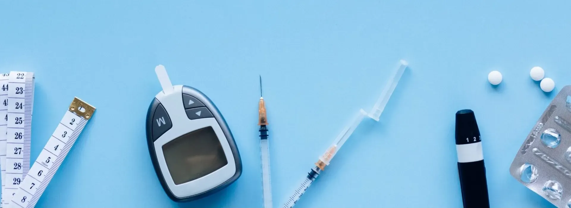 Diabetes mellitus: Ein Blutzuckermessgerät, Insulinspritzen und Tabletten auf einem blauen Untergrund